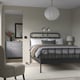 Modern bedroom with STJÄRNÖ black bed, white linens, pendant light, black lamps, grey dresser, mirror, beige chair, grey rug.