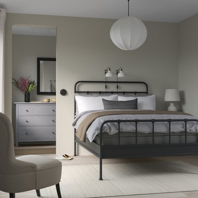 Modern bedroom with STJÄRNÖ black bed, white linens, pendant light, black lamps, grey dresser, mirror, beige chair, grey rug.
