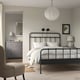 Modern bedroom with black curved bed, white linens, pendant lamp, grey walls, dresser, and armchair.