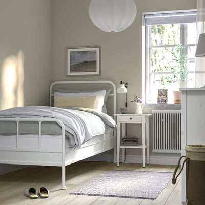 Minimalist bedroom with white bed, bedside table, and decor.