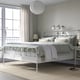 White STJÄRNÖ metal bed, classic design, by window with grey curtains.