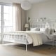 STJÄRNÖ metal bed, curved headboard, large with neutral bedding, by window with lamp & rug.