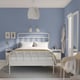 Minimalist bedroom: white bed, beige bedding, grey rug, blue walls, light, art, clock, chair, jacket.