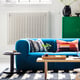 Modern living room: blue stockholm sofa, color-block pillows, patterned rug, black side table, green cabinet, white radiator.