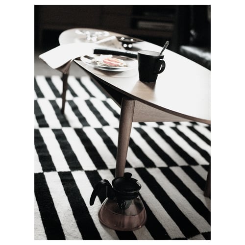 Black and white striped rug under a wooden table with plates and a mug on top.