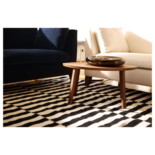Modern living room with black and white striped rug, wooden coffee table, black couch, and beige chair.