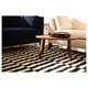 Modern living room with black and white striped rug, wooden coffee table, black couch, and beige chair.