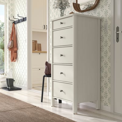 Modern white STOREMOLLA chest with six drawers in entryway, between floral wall and door, with hanging organiser left and small stool/rug front.