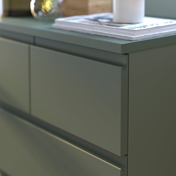 Modern green chest with drawers, stylish handles, and neatly arranged books and a cup on top.