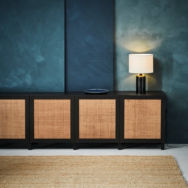 Black sideboard with woven natural fibre doors, white lamp, blue wall.