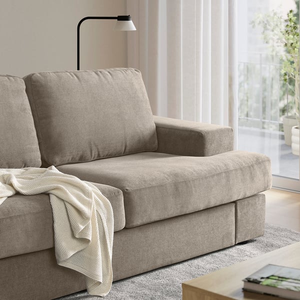 Beige SUNDBRON sofa chair with cushions and blanket, fitting in a bright living room.