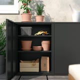 Black SUNDSÖ cabinet stores terracotta pots and gardening tools.