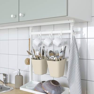 Kitchen storage: utensils in hanging pots, mugs, and towel on rail below cabinet.