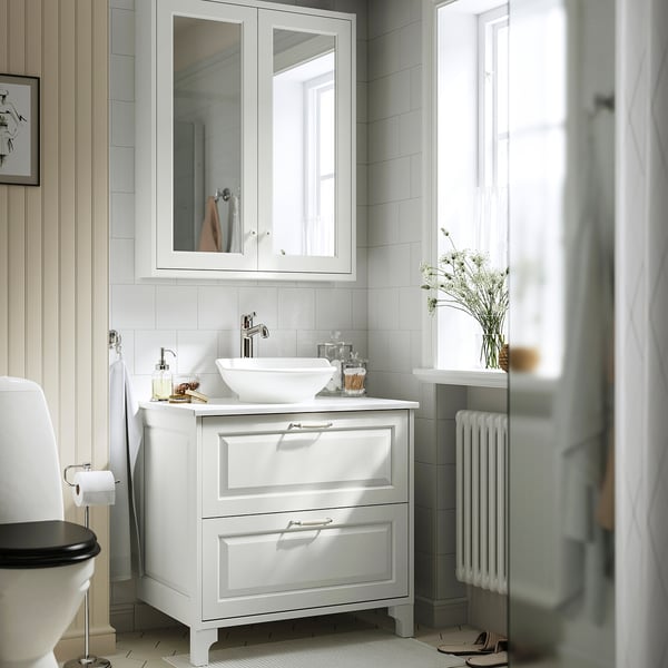 White vanity with sink, mirror, and toilet. Classic design with bevelled panels.