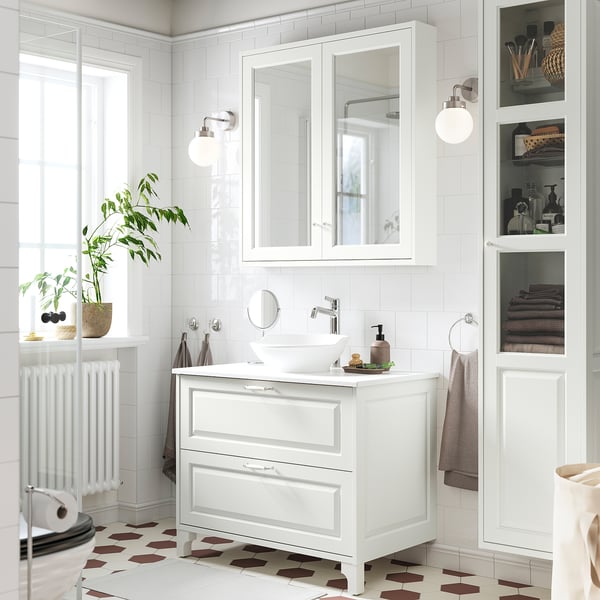 White TÄNNFORSEN vanity with ceramic basin, 2 drawers, wall cabinet, mirrored door, wall lights, tiled room with plants.