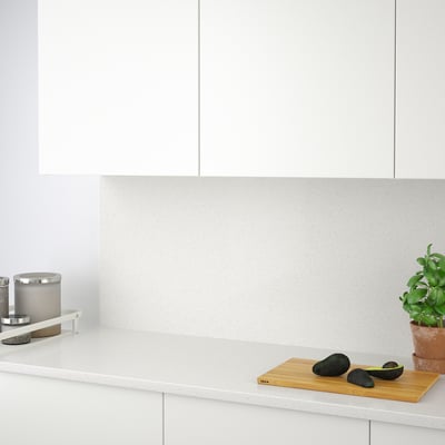 Minimalist kitchen with recycled glass backsplash protecting walls, resistant to moisture and stains. Avocados and plant on countertop.