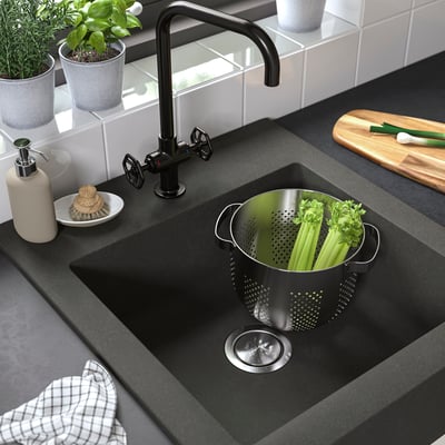 Modern dark grey sink with high tap and colander of fresh veggies.