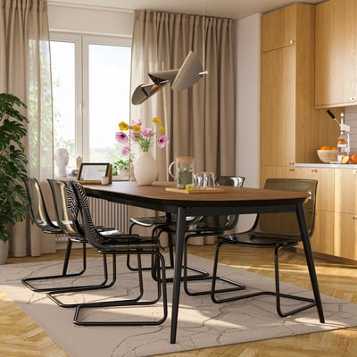 Modern dining area with TOBIAS black chairs, wooden table, hanging lamp, and flower vase; spacious, light-filled room.