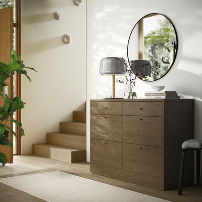 Wooden chest with 6 drawers, mirror, plant, staircase.