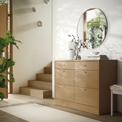 Wooden dresser in hallway, 6 drawers, mirror, plant, stairs.