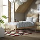 A modern bedroom with a TONSTAD light oak bed, light blue linens, cosy alcove, geometric rug, coffee maker, pendant lamps, and a large plant.