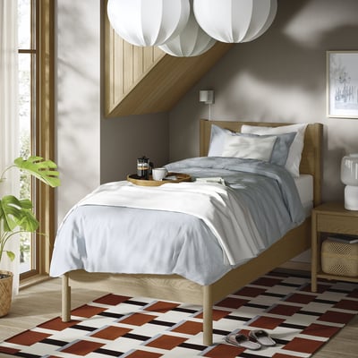 TONSTAD bed in neutral tones, wooden frame, white linens, modern design, large, with chequered rug, plants, large lamps, grey walls.