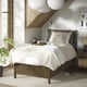Modern wooden bed with white bedding, hanging lights, and plant.
