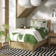 Bedroom with TONSTAD light wood bed, green leaf print linens, black-white rug, large plant, hanging lamps, white walls.