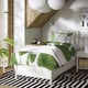 Bright, white bed with green leafy bedding, black and white striped rug, hanging lights, and potted plant beside a window.