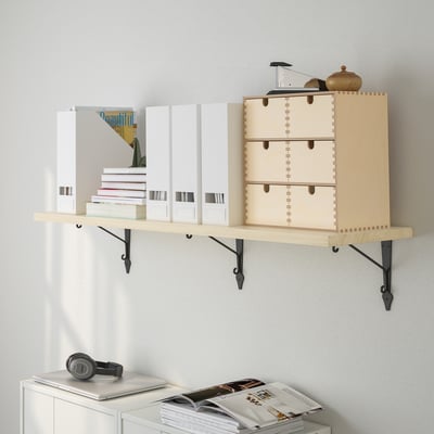 Wooden wall shelf holding boxes and books, with a light wood finish and black metal brackets. Display items include headphones and a vase.