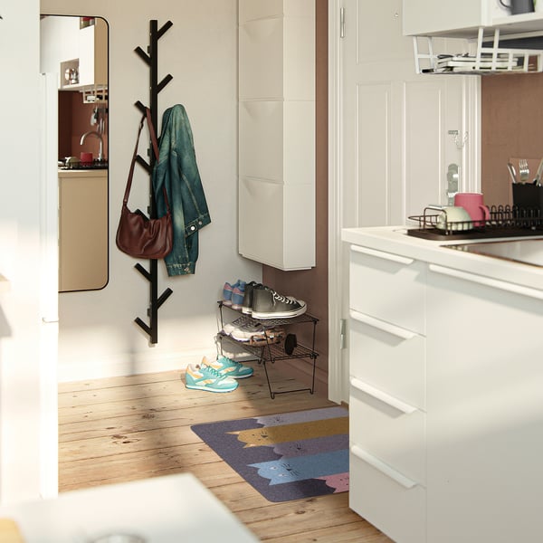 Contemporary entryway with white cabinets, black hooks, and a colourful rug. Brown purse, denim jacket, and blue trainers are neatly placed.