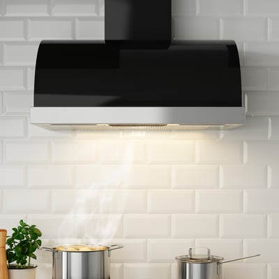 Modern kitchen with black and stainless steel hood venting steam, surrounded by white tiles.