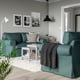Modern living room with teal green UPPLAND sofa, pillows, black lamp, white rug, and wall art. The sofa is large yet fits well in the space.