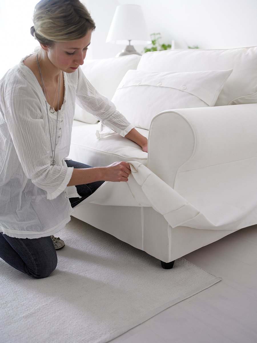 A person is arranging white UPPLAND sofa bed with removable, machine-washable cotton covers.