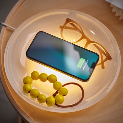 White bowl on wood table, holding: phone, glasses, beads.