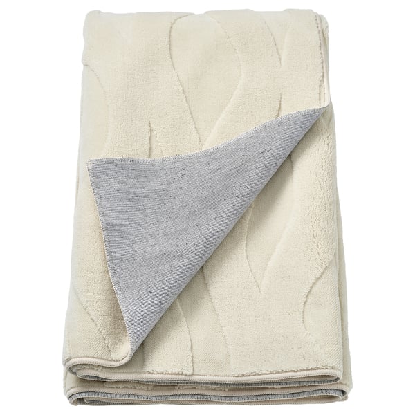Folded cream-colored vaxelfel rug with a soft, textured leaf pattern and grey backing, primarily made of recycled polyester.