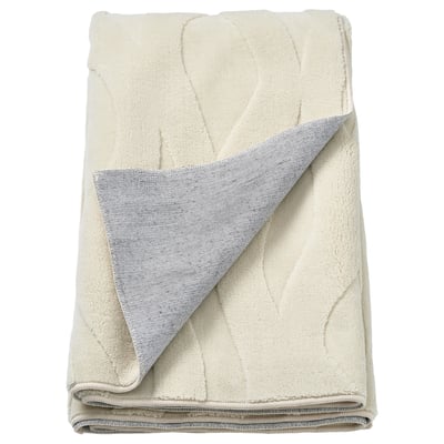 Folded cream-colored vaxelfel rug with a soft, textured leaf pattern and grey backing, primarily made of recycled polyester.