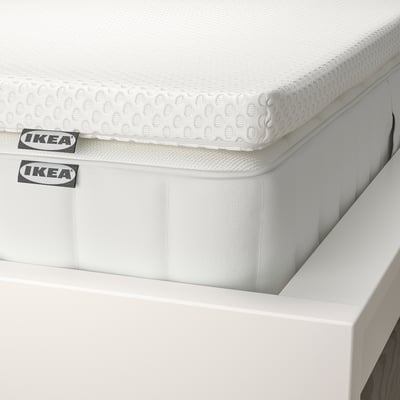 Close-up of a thick, white ikea mattress with textured top, neatly placed on a white bed frame.