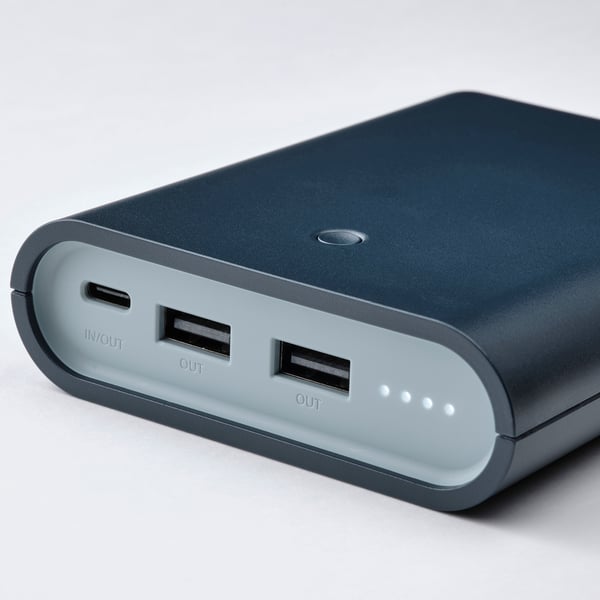 Portable power bank with two usb-a and one usb-c port, all neatly arranged and clearly labelled on a smooth, dark grey surface.