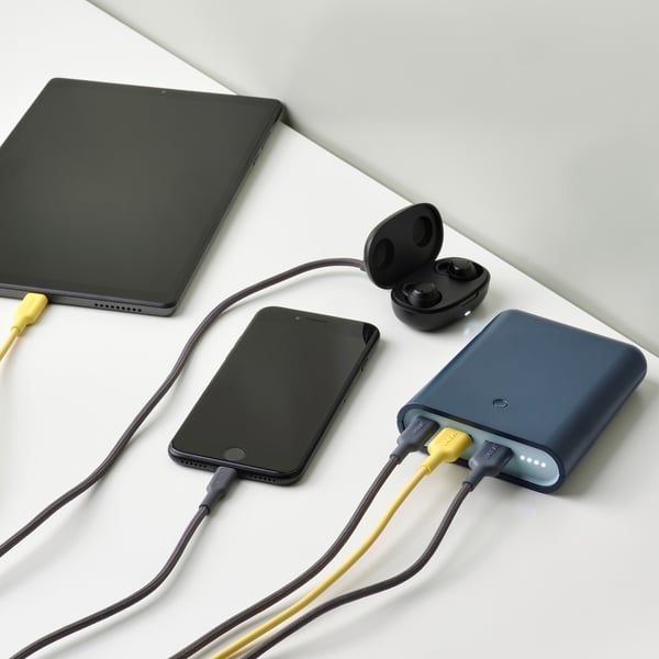Power bank charging three devices: smartphone, tablet, and earbuds.