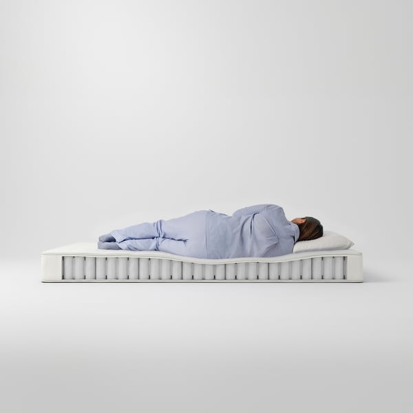 Person laying on VESTERÖY mattress, light blue pyjamas, on white background.