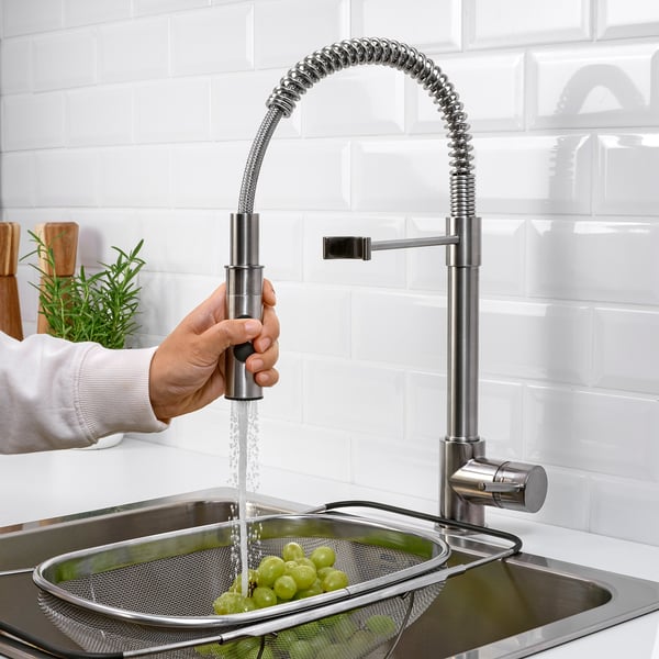 A sleek stainless steel tap with a handheld sprayer in action, rinsing grapes in a strainer under a modern kitchen sink.