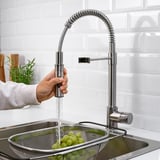 A sleek stainless steel tap with a handheld sprayer in action, rinsing grapes in a strainer under a modern kitchen sink.
