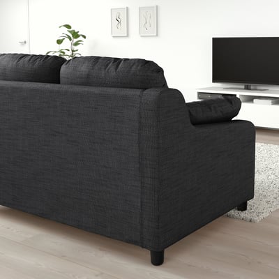 Modern black sectional sofa in minimalist living room with tv, rug, and plant.