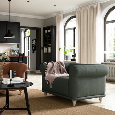 Modern living room with green VISKAFORS armchair, soft cushions, beige curtains, and black coffee table with candles and books.