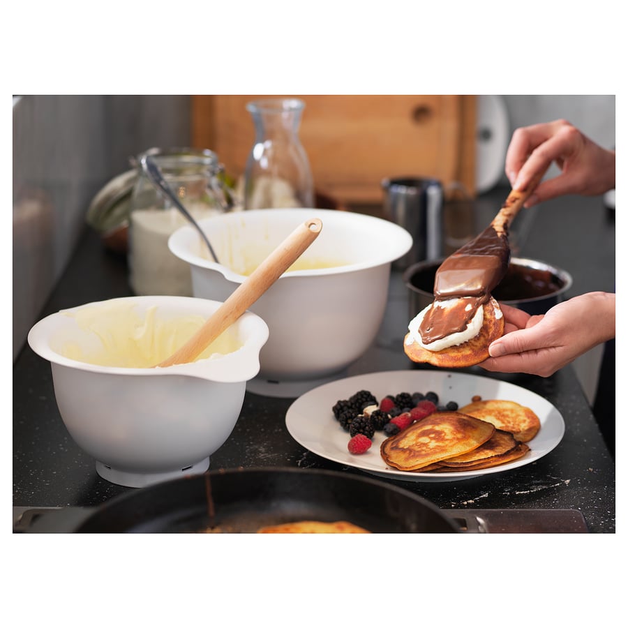 Person prepares pancakes and spreads chocolate sauce using VISPAD mixing bowls on kitchen counter.