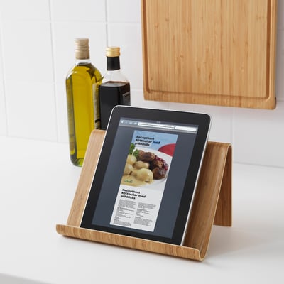 A tablet displaying a recipe in a bamboo stand on a kitchen counter. Olive oil and vinegar bottles in the background.