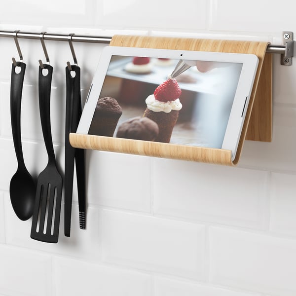Tablet and cookbook holder mounted on kitchen wall rail, freeing counter space, displaying recipe on screen.