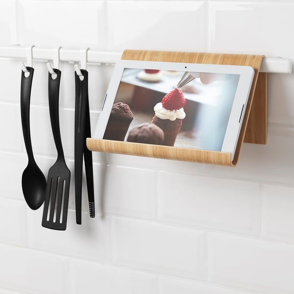 Tablet and cooking utensils holder on wall, displaying dessert recipe and hanging spatula, ladle, and tong.