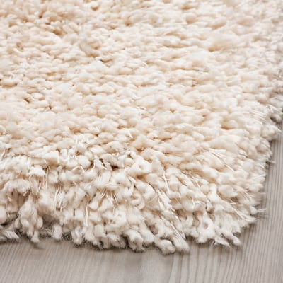 A close-up of a luxurious, shaggy white rug on a wooden floor, showcasing its soft, textured pile.